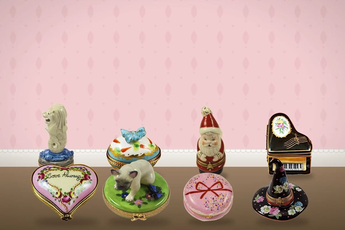 Eight hand-painted Limoges boxes grouped on a table, including a heart, a piano, a witch's hat, a pink macaron and a Santa.